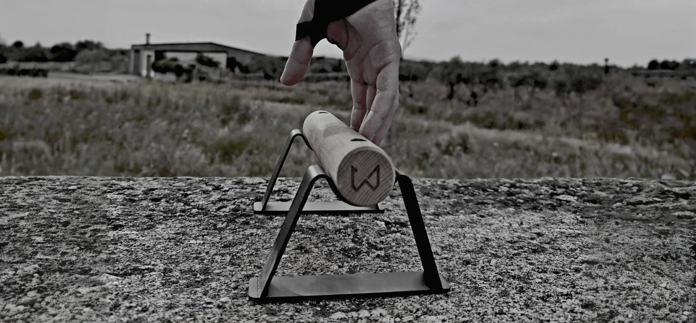 Hand reaching for a wooden parallette bar with black metal stands on a textured concrete surface.