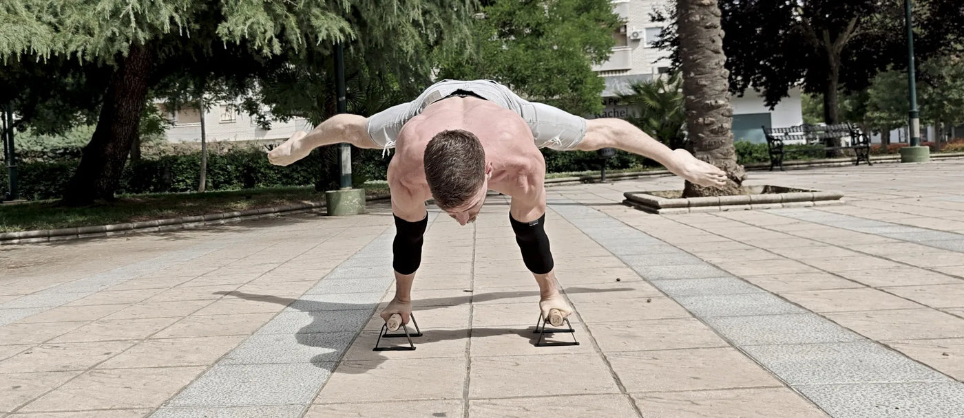 Muscular man performing a calisthenics handstand with wide-spread legs outdoors.