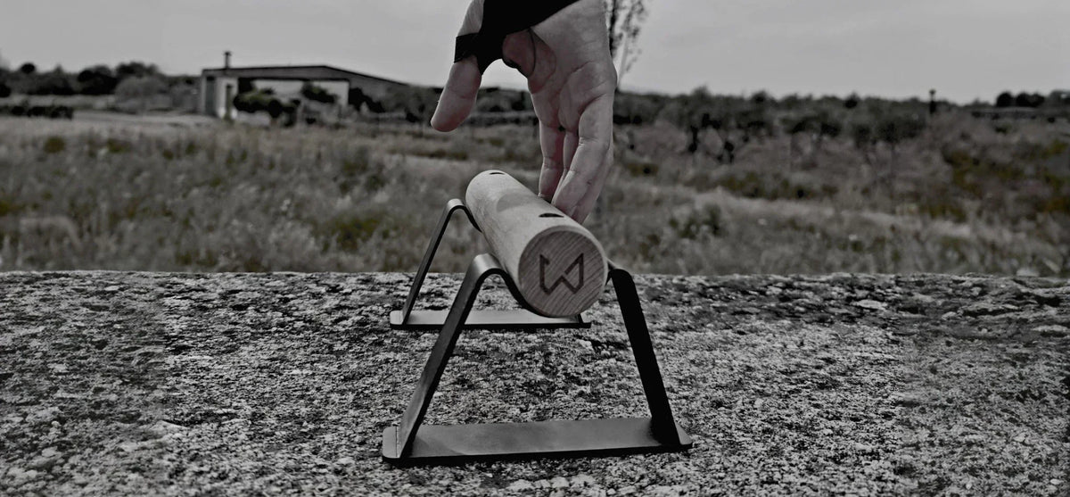 Hand reaching for a wooden parallette bar with black metal stands on a textured concrete surface.