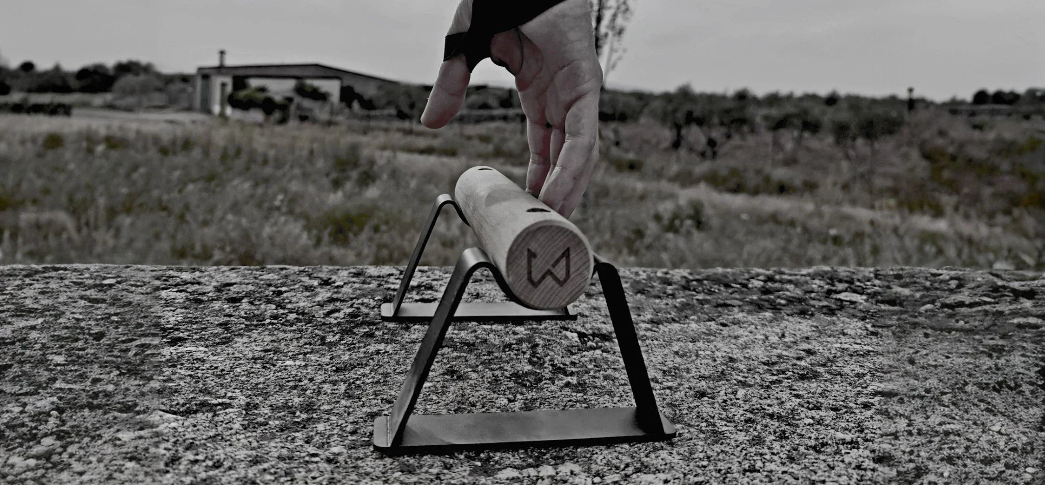 Hand reaching for a wooden parallette bar with black metal stands on a textured concrete surface.