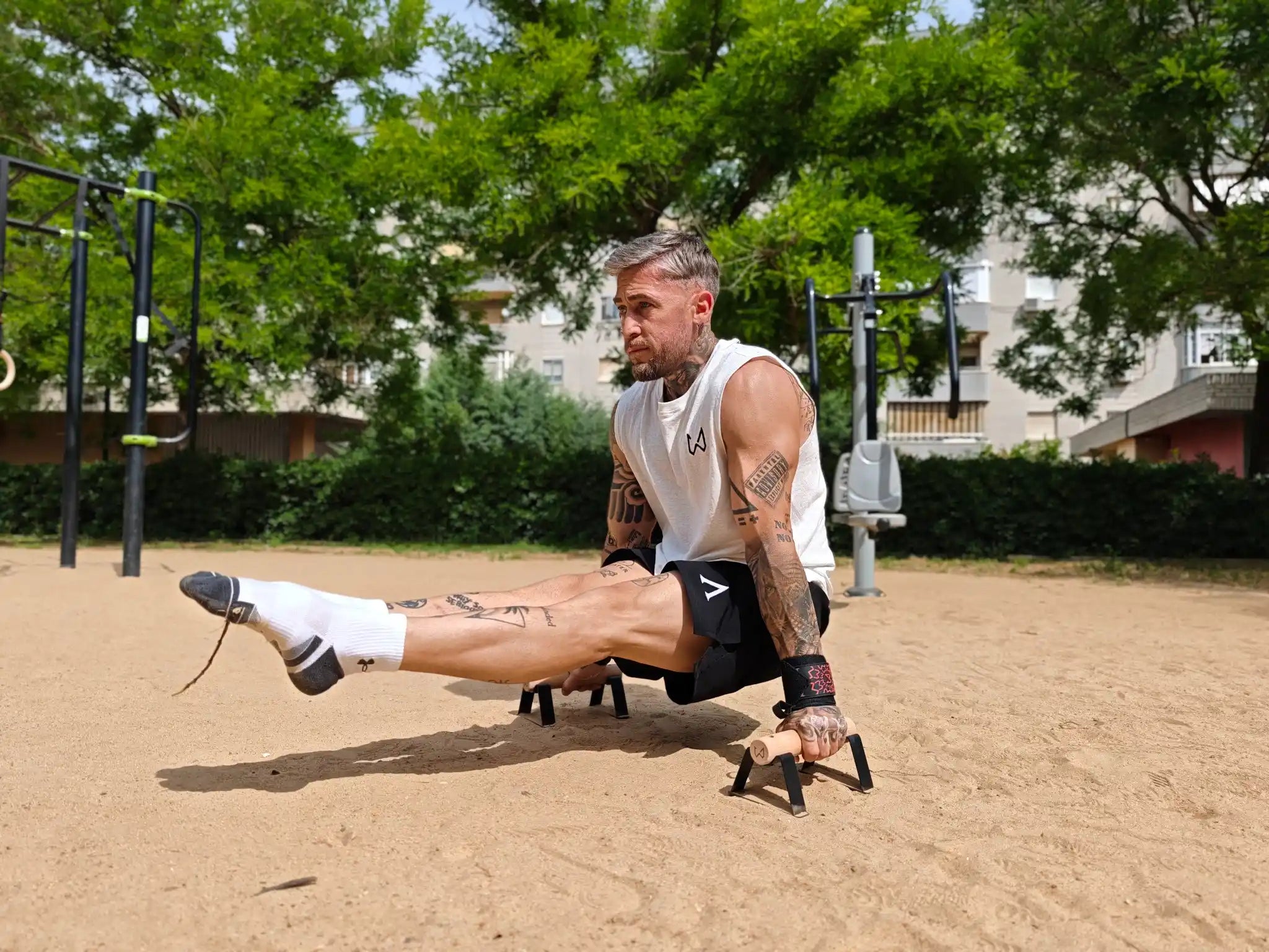 Man performing a calisthenics L-sit on wooden parallettes in an outdoor park.
