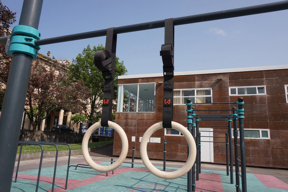 Exercise rings hanging from a metal bar outdoors with a building in the background