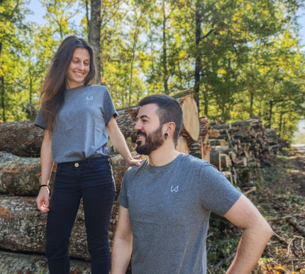 Two people standing in a forest with stacked logs around them wearing hemp and organic cotton tshirt.