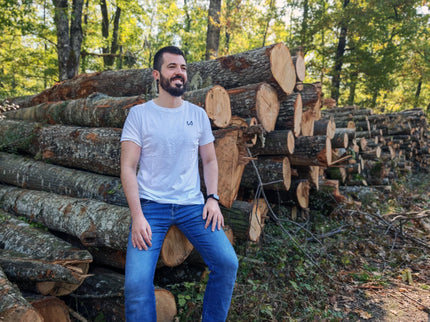 Man sitting among stacked logs in a forest wearing hemp and organic cotton tshirt.