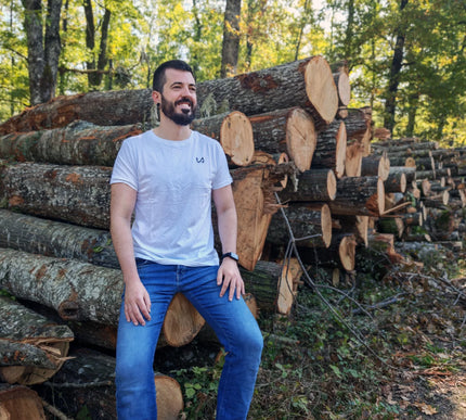 Man sitting among stacked logs in a forest wearing hemp and organic cotton tshirt.