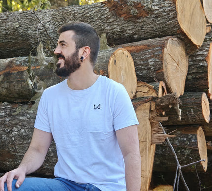 Man sitting among stacked logs wearing a white t-shirt with a logo of wild dynamics