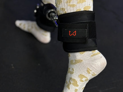 Person wearing a black ankle strap with a visible brand logo on a dark background