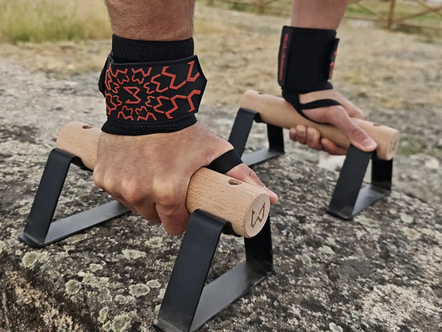 A close up of hands wearing wrist wraps holding a pair of parallettes