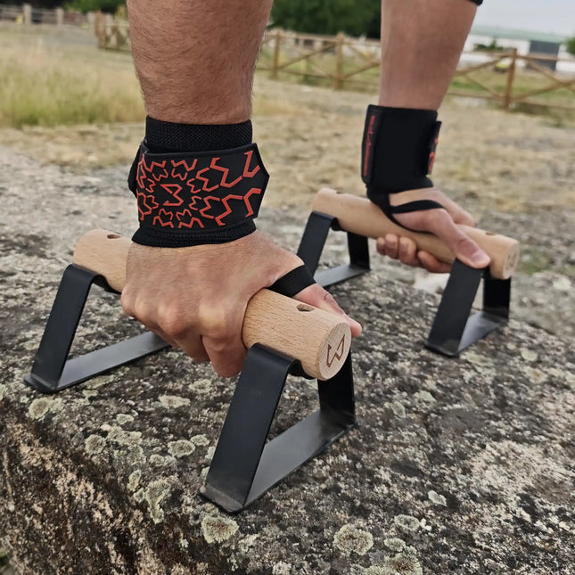 A close up of hands wearing wrist wraps holding a pair of parallettes