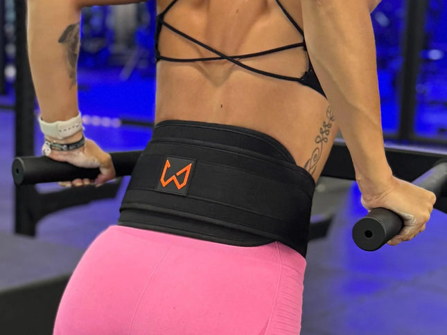 Person exercising with a black dip belt featuring an orange logo in a gym setting.