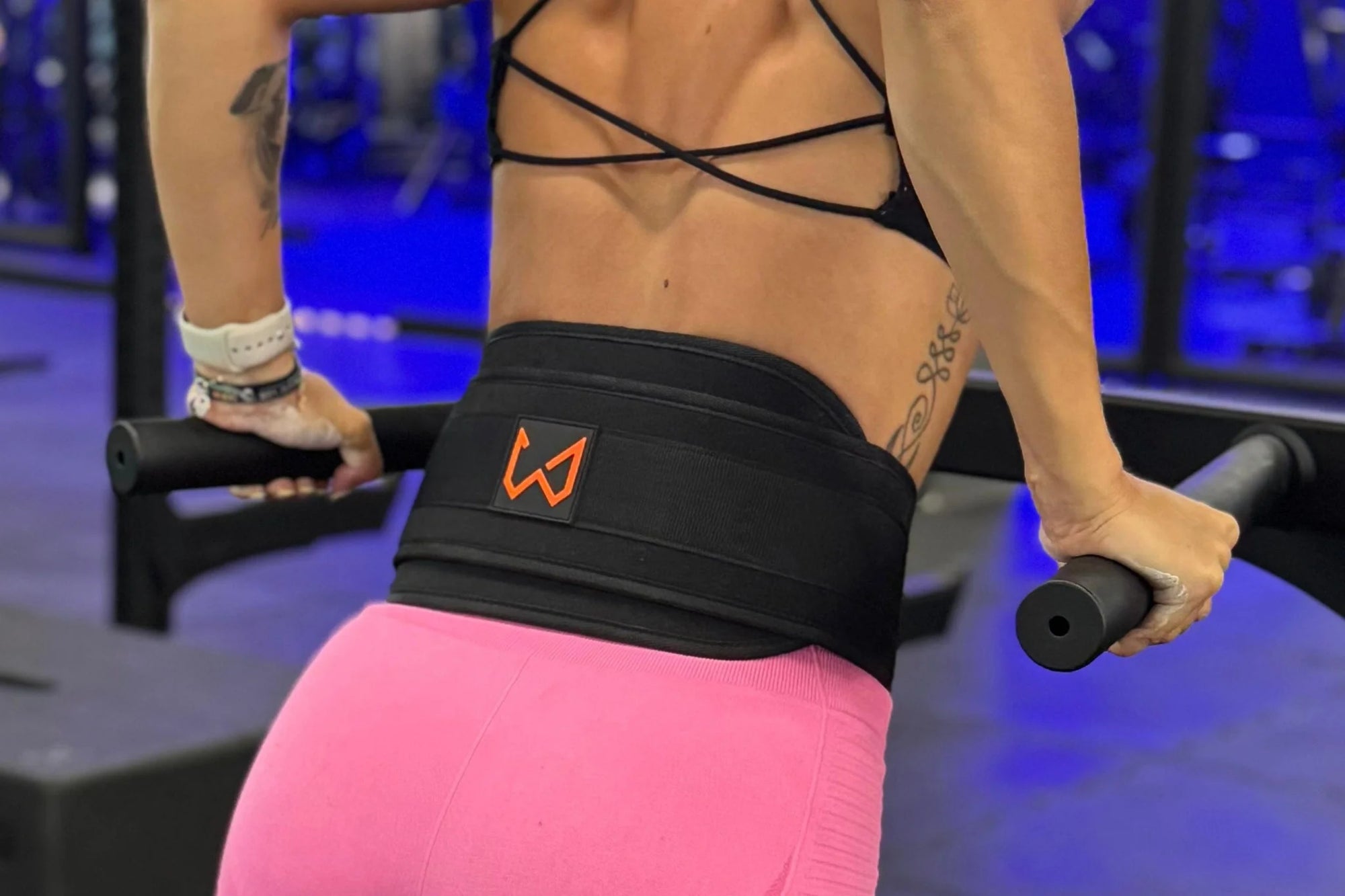 Person exercising with a black dip belt featuring an orange logo in a gym setting.
