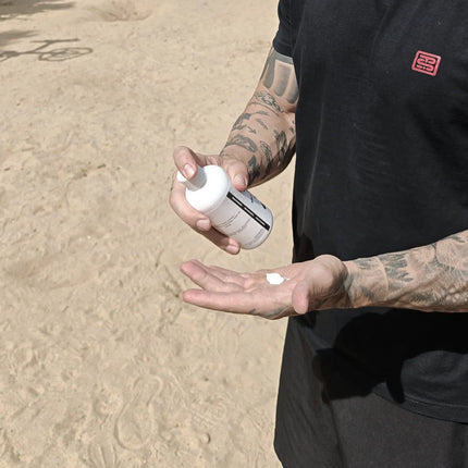 Person applying liquid chalk to hands outdoors on a sandy surface
